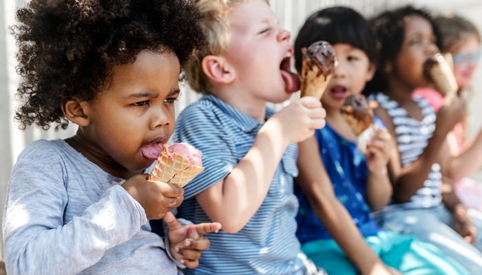 Grupo de niños pequeños sentados comiendo conos de helado